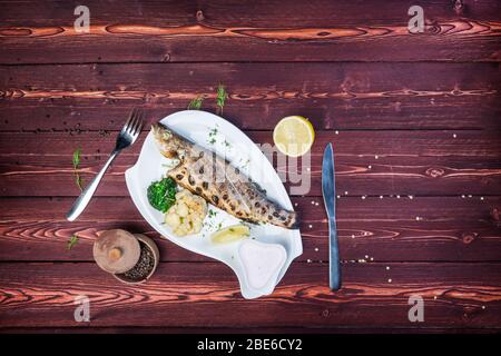 Gegrillter Wolfsbarsch auf einem Teller. Gesunde Ernährung. Serviert Blumenkohl und Broccoli. Es gibt einen schwarzen Pfeffer und Besteck. Draufsicht Stockfoto