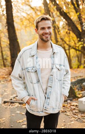 Bild von schönen jungen kaukasischen Mann in Denim Jacke lächelnd beim Spaziergang im Park Stockfoto