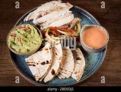 Chicken Sie Fajitas mit gegrillten Zwiebeln und Paprika und mit Mehltortillas auf ländlichen Holzbrett servieren Stockfoto