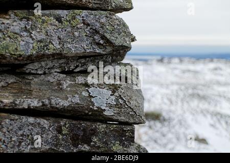 Flechten bedeckten Felsen cairn Nahaufnahme mit verschwommenem Berghintergrund in Norwegen, auf dem Weg nach Vidden, skandinavische Natur im Winter Stockfoto