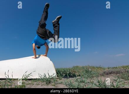 Ein Mann macht Stunts auf einem weißen Boot auf dem Sand. Es gibt Pflanzen im Sand. Der Himmel ist klar und blau. Stockfoto