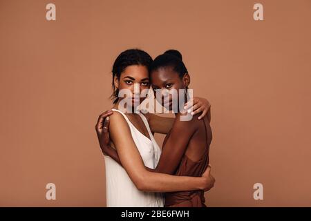Zwei verschiedene Freundinnen vor braunem Hintergrund umarmen sich Stockfoto