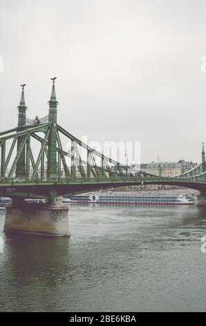 Budapest, Ungarn - 6. Nov 2019: Freiheitsbrücke über die Donau an einem nebligen, regnerischen Herbsttag. Kreuzfahrtschiff und historisches Zentrum im Hintergrund. Vertikales Foto. Ungarische Hauptstadt Stadtbild. Stockfoto