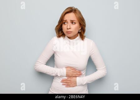 Gesundheit Probleme Konzept. Frau, die an Magenschmerzen leidet, Bauchschmerzen oder Krämpfe fühlt, isoliert auf blauem Hintergrund. Periode Menstruation, Stockfoto