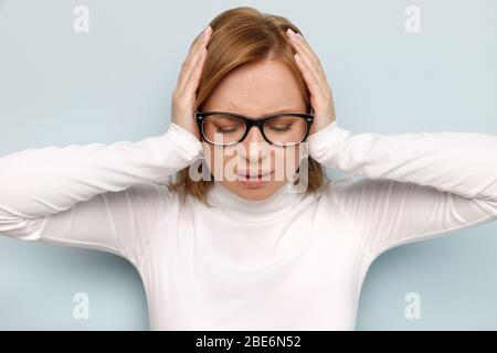 Verärgerte Geschäftsfrau in Brille schließt Ohren, schließt die Augen, versucht ruhig zu bleiben und die Kontrolle über Emotionen zu übernehmen, hört nicht, kann sich nicht konzentrieren, isoliert Stockfoto