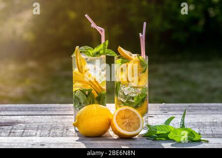 Sommerkonzept. Hausgemachte Limonade mit Zitrone, Minze und Eis in Gläsern, auf Holztisch, im Freien, getöntes Bild. Stockfoto