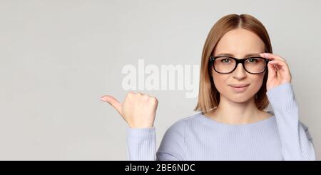 Nahaufnahme Porträt der erfolgreichen europäischen Frau mit Brille, zeigt mit Daumen an leere Kopie Raum, zeigt Platz für Ihre Anzeige, isoliert Stockfoto