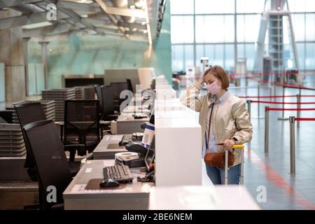 Frau mit Gepäck über Flugannullierung, steht an leeren Check-in-Schaltern am Flughafenterminal wegen Coronavirus-Pandemie/Covid-19-Ausbruch Trave Stockfoto