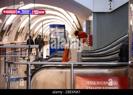 St. Petersburg, Russland - 05. April 2020. Frau Passagier trägt rote Schutzmaske steigt auf Rolltreppe.Fast leer Station der St. Petersburg U-Bahn d Stockfoto