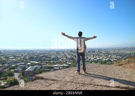 Junger Mann steht am Rande des Hügels und öffnet Arme mit der beeindruckenden Stadtansicht Stockfoto