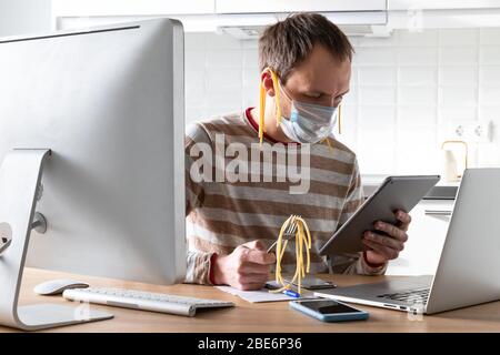 Mann im Gesicht Maske mit Nudeln auf den Ohren, hält eine Gabel und liest gefälschte / breaking Nachrichten und eine Rede des Präsidenten auf Tablet über Coronavirus während Stockfoto