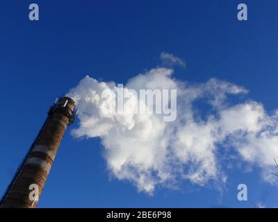 Rohre einer alten Fabrik werfen Wolken von giftigem weißem Rauch in den Himmel, die die Atmosphäre schädigen. Urbaner Smog aus Rauch aus Kesselhäusern. Weißer Rauch aus einem Kamin gegen einen blauen klaren Himmel. Stockfoto