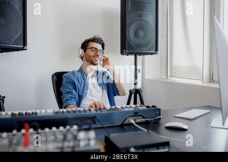 Männlicher Musik-Arrangeur komponiert Lied auf Midi-Piano und Audio-Equipment im digitalen Aufnahmestudio. Man produziert elektronischen Soundtrack oder Track in Stockfoto