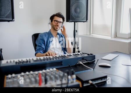 Männlicher Musik-Arrangeur komponiert Lied auf Midi-Piano und Audio-Equipment im digitalen Aufnahmestudio. Man produziert elektronischen Soundtrack oder Track in Stockfoto