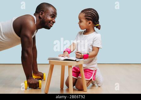 Schwarzer Vater macht Liegestütze, seine Tochter nimmt Notizen. Stockfoto