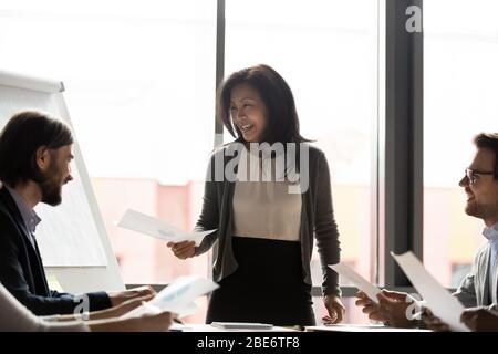 Lächelnder asiatischer Teamleiter teilt Handzettel bei der Besprechung Stockfoto