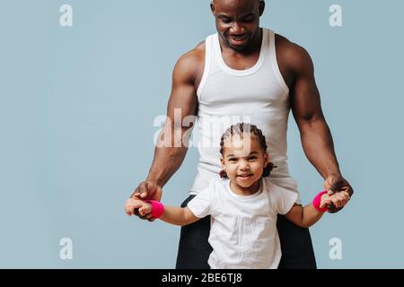 Vater und Tochter in sportlicher Kleidung zeigen Muskeln über blau Stockfoto