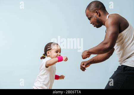 Vater Sparring mit seiner kleinen Tochter, die ernsthafte Gesicht. Über blau Stockfoto