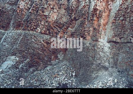 Natürliche Basaltsteinwand mit Rissen und Spalten mit einer roten Farbe aus Eisen. Gesteinsstruktur. Wand aus Graphit-Stein. Steinhintergrund. Stockfoto