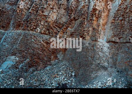 Natürliche Basaltsteinwand mit Rissen und Spalten mit einer roten Farbe aus Eisen. Gesteinsstruktur. Wand aus Graphit-Stein. Steinhintergrund. Stockfoto