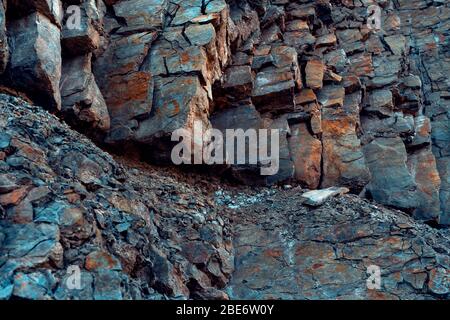 Natürlicher Basaltgestein mit Rissen und Spalten mit einer roten Farbe, die aus Eisen stammt. Struktur der Felswand. Wand aus Graphit-Stein. Steinhintergrund. Stockfoto