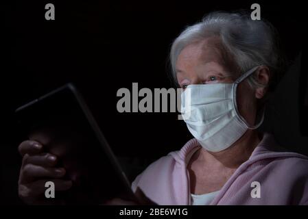 Ältere Frau mit Gesichtsmaske chats mit Tablet-Computer Stockfoto
