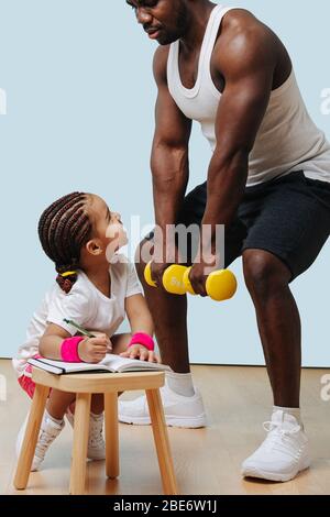 Schwarzer Vater hockt, seine Tochter nimmt sich Notizen. Stockfoto