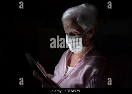 Ältere Frau mit Gesichtsmaske chats mit Tablet-Computer Stockfoto
