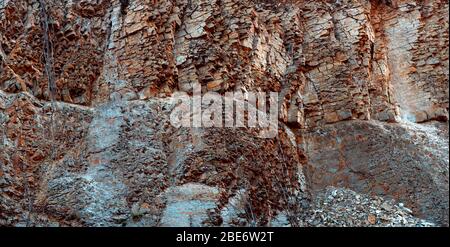 Natürliche Basaltsteinwand mit Rissen und Spalten mit einer roten Farbe aus Eisen. Gesteinsstruktur. Wand aus Graphit-Stein. Steinhintergrund. Stockfoto