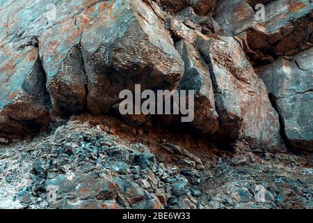 Natürlicher Basaltgestein mit Rissen und Spalten mit einer roten Farbe, die aus Eisen stammt. Struktur der Felswand. Wand aus Graphit-Stein. Steinhintergrund. Stockfoto