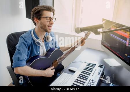 Man spielt Gitarre und Gesang und produziert elektronischen Soundtrack oder Track in Projekt zu Hause. Männlicher Musik-Arrangeur komponiert Lied auf Midi-Klavier und Audio Stockfoto