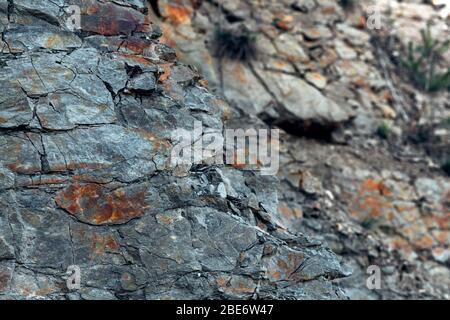 Natürlicher Basaltgestein mit Rissen und Spalten mit einer roten Farbe, die aus Eisen stammt. Struktur der Felswand. Wand aus Graphit-Stein. Steinhintergrund. Stockfoto