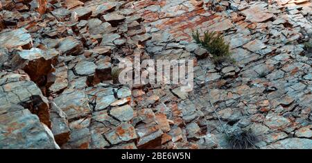 Natürliche Basaltsteinwand mit Rissen und Spalten mit einer roten Farbe aus Eisen. Gesteinsstruktur. Wand aus Graphit-Stein. Steinhintergrund. Stockfoto