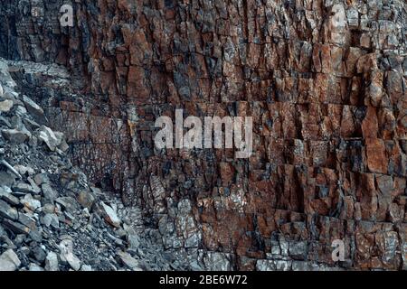 Natürliche Basaltsteinwand mit Rissen und Spalten mit einer roten Farbe aus Eisen. Gesteinsstruktur. Wand aus Graphit-Stein. Steinhintergrund. Stockfoto