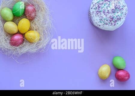 Ostereier in einem provisorischen Nest auf violettem Hintergrund, daneben ist Osterkuchen und drei Eier Stockfoto
