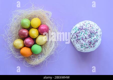 Ostereier in einem provisorischen Nest auf violettem Hintergrund, neben dem Osterkuchen Stockfoto