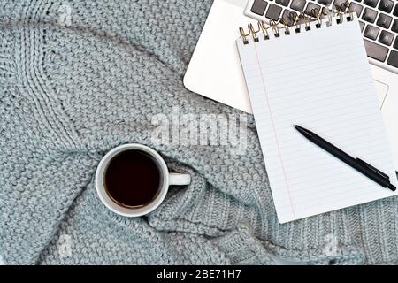 Flatlay von gemütlichen Arbeits Schreibplatz mit warmen Pullover Kaffee, Laptop und Schreibzubehör. Arbeit von zu Hause. Schreiben. Warmes Konzept bei kaltem Wetter. Stockfoto