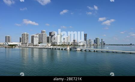 Miami, Florida - 4. April 2020 - Skyline der Stadt Miami und Venetian Causeway spiegeln sich im noch blauen Wasser der Biscayne Bay unter morgendlicher Wolkenlandschaft wider. Stockfoto