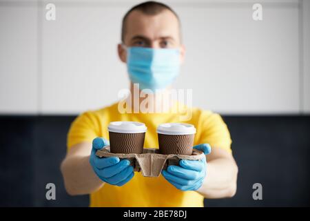 Kurier in Schutzmaske und medizinischen Handschuhen liefert Essen und Kaffee zum Mitnehmen. Lieferservice unter Quarantäne, Krankheitsausbruch, Coronavirus covi Stockfoto