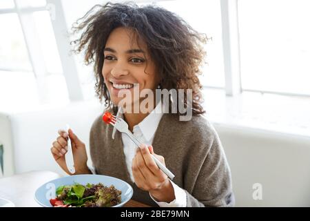 Porträt der jungen schönen afroamerikanischen Frau Salat essen, während das Mittagessen im Café Stockfoto