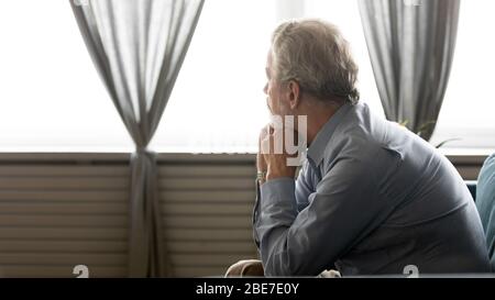 Rückansicht trauriger älterer Mann, der im Fenster schaut und alleine sitzt Stockfoto