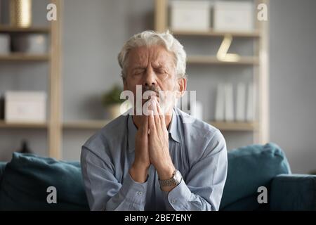 Trauriger älterer Mann mit geschlossenen Augen, der mit Hoffnung betet Stockfoto