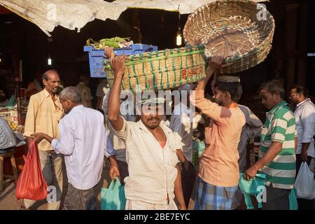 Träger, die Körbe auf dem Kopf tragen, und Käufer auf dem Crawford Market (Mahatma Jyotiba Phule Market), einem großen Obst- und Gemüsemarkt in Mumbai, Stockfoto