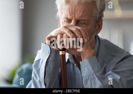 Nahaufnahme traurig älteren Mann, der die Hände auf Gehstock Stockfoto