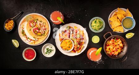 Mexikanisches Essen, ein flaches Panorama auf schwarzem Hintergrund. Nachos, Tortillas, Paloma Cocktails, Guacamole, aufgenommen von oben Stockfoto