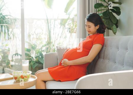 Schöne junge asiatische Frau ist glücklich, sich um neugeborenes Kind in Zukunft zu nehmen. Modernes gesundes Mama Konzept. Stockfoto