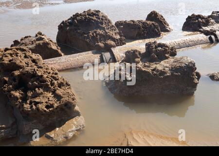 Alte Abschnitte des Abwasserrohrs zeigten sich nur bei außergewöhnlich niedrigen Gezeiten an einem lokalen Strand, der nun stillgelegt und der Natur überlassen wurde. Stockfoto