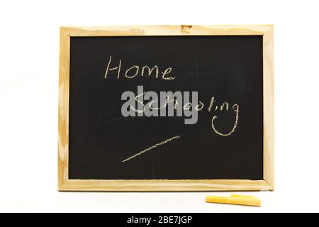 Kleine Tafel mit den Worten Home Schooling, die mit Kreide auf einem klaren Hintergrund in horizontalem Format isoliert darauf geschrieben sind Stockfoto