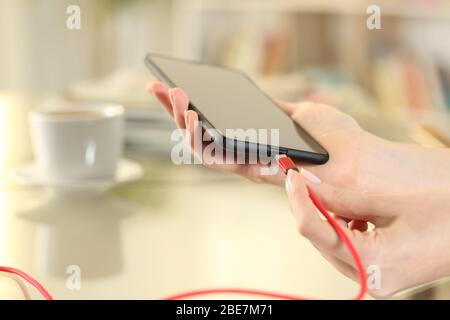 Nahaufnahme einer Frau, die das usb-Kabel des Akkuladegeräts an das Smartphone ansteckt und zu Hause auf einem Schreibtisch sitzt Stockfoto