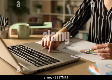 Nahaufnahme der Unternehmer Hände Vergleich Graph Bericht in der Nacht auf Laptop im Home Office Stockfoto